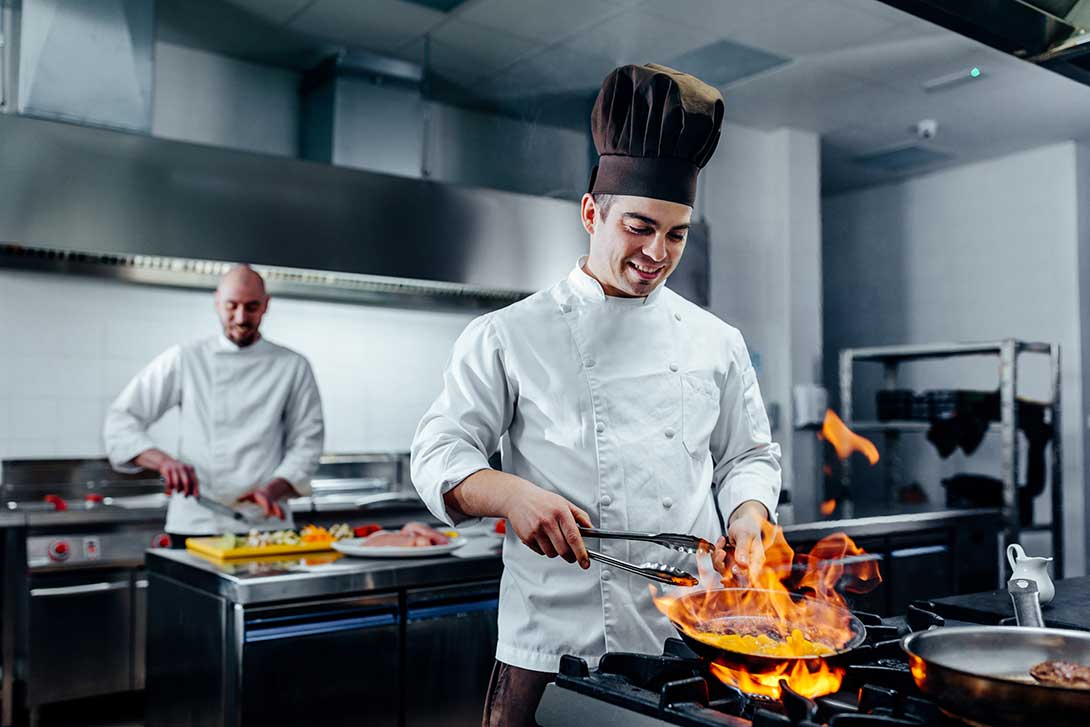 Two chefs in a kitchen cooking on a gas cooktop