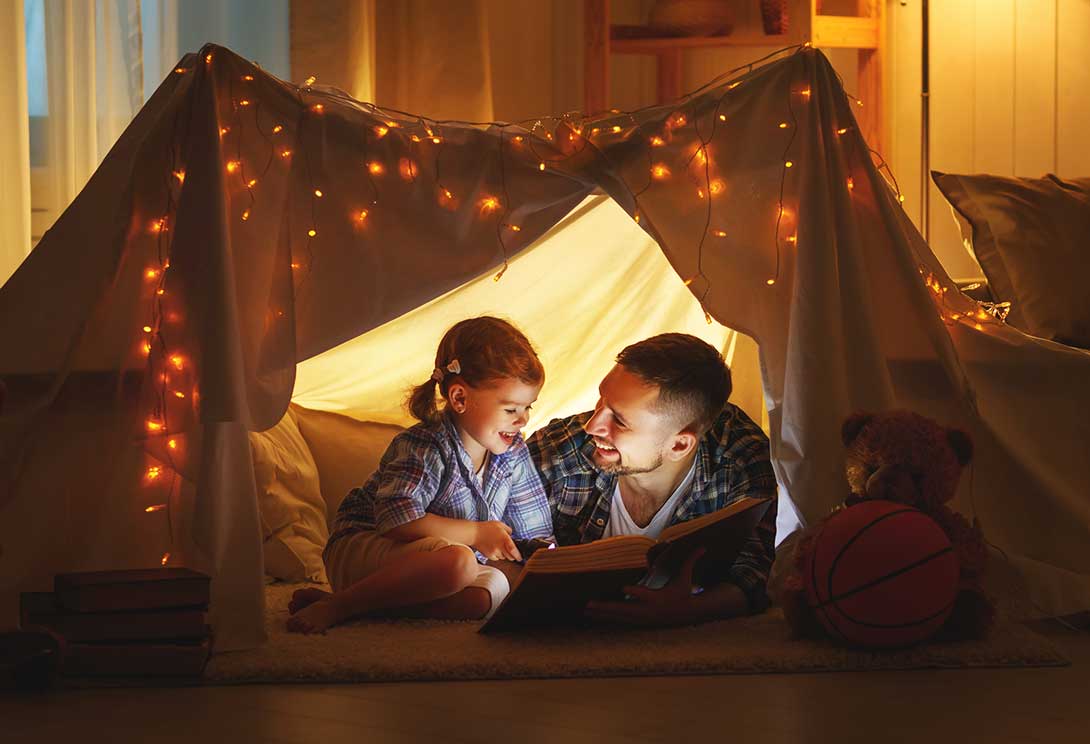 Father and daughter reading a book in an indoor tent