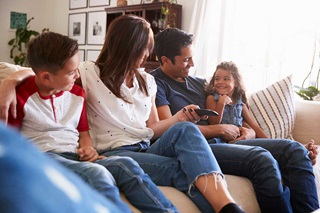Family of mom, dad, one young girl and one young boy sitting together on a couch and smiling