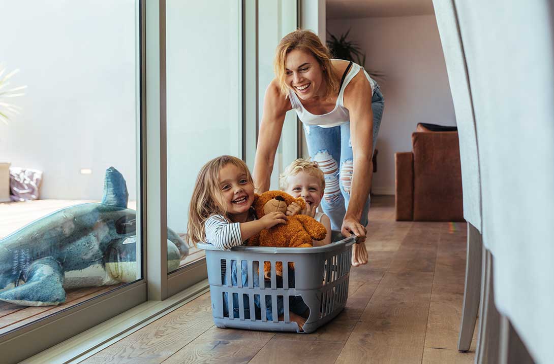 Mom pushing children down hallway in a laundry basket