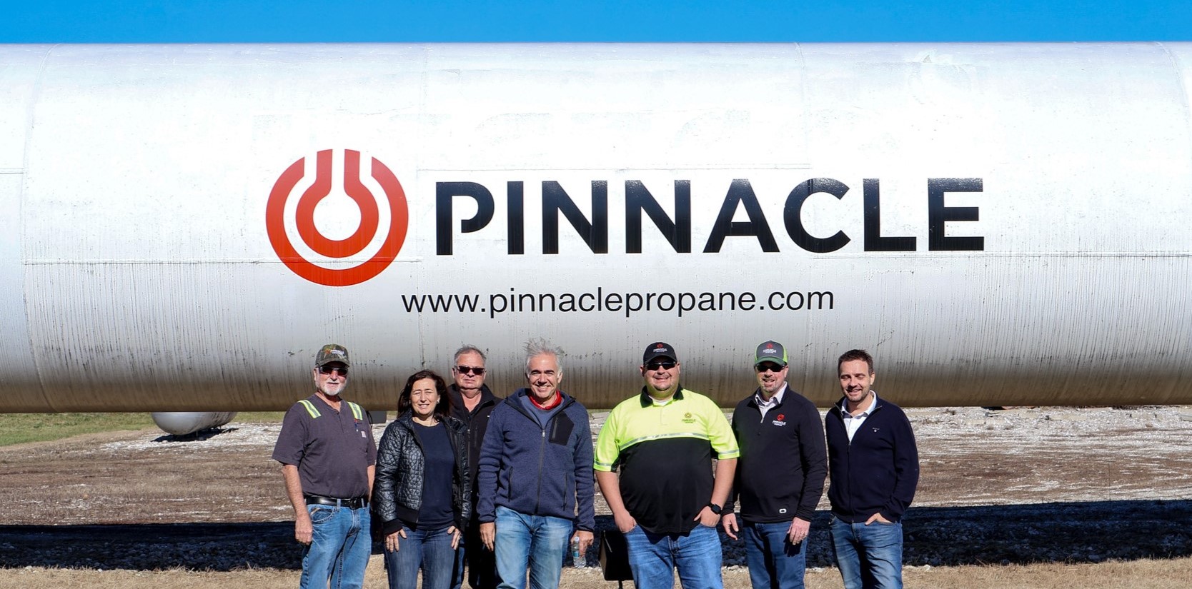 Pinnacle Propane commercial solutions team in front of a large branded bulk propane tank under a clear blue sky
