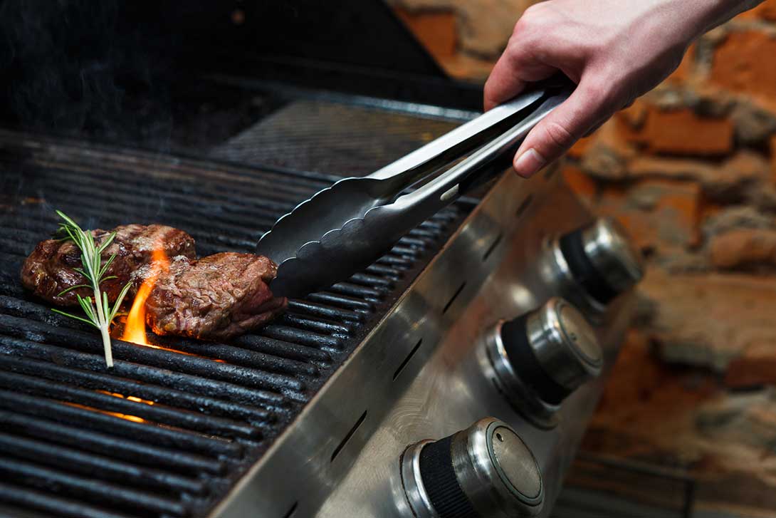 Person grilling meat on an outdoor grill