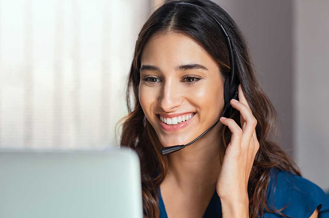 Smiling woman on headset telephone in front of a computer