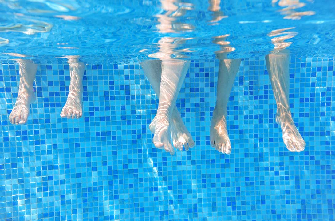 People's legs dangling in swimming pool